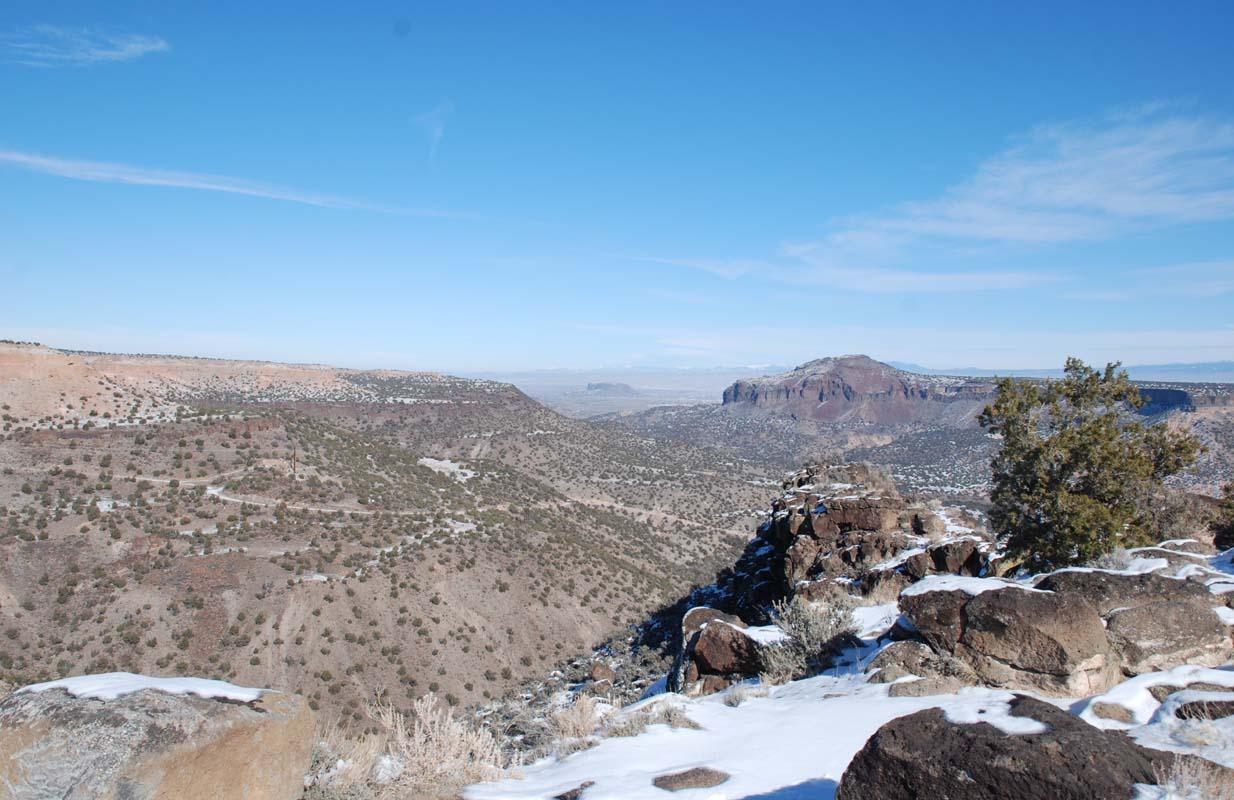 Vast desert landscape featuring rocky hills and sparse vegetation under a clear blue sky