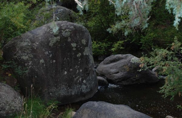 Large, moss-covered boulders frame a tranquil stream, surrounded by lush greenery